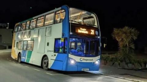 A blue, white and green bus travelling along a road at night
