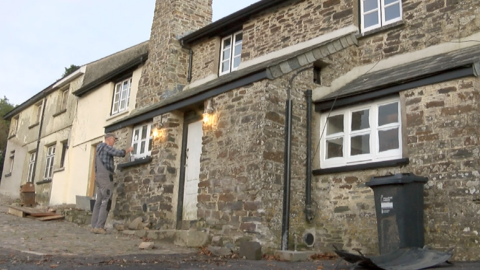 A large granite building with a man in grey overalls and a blue flannel shirt painting one of the window frames white.