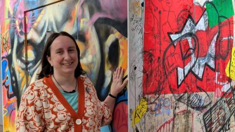 Sarah Keeling standing next to a replica of a modern cell. It has been decorated in different kinds of graffiti on the outside. 