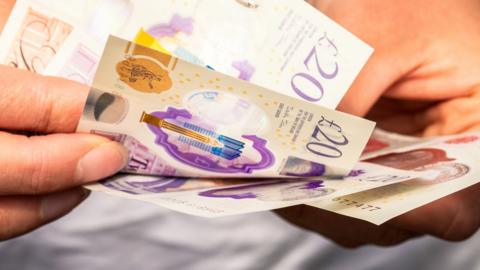 A close up image of a woman's hands as she prepares £20 banknotes to pay with.