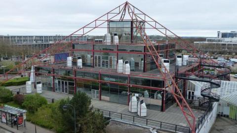 The reflective glass pyramid structure that is The Point in Milton Keynes. It has its edges lined by red metal frames.