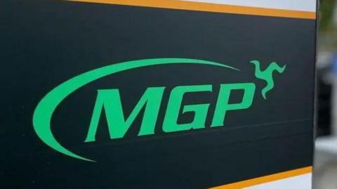 A close up of a sign that reads MGP in green writing on a black background, the three legs of man.