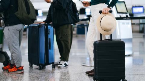 Cropped shot of group of airline passengers with suitcases standing in queue, waiting at check-in counter at International airport. Ready for a trip. Business travel. Travel and vacation concept - stock photo
