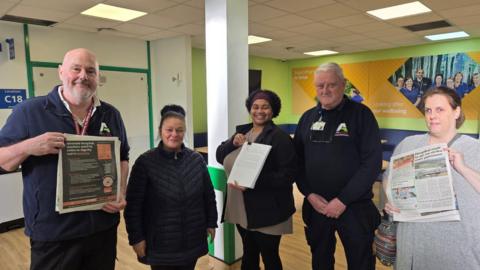 A line-up of five men and women with the lady in the middle holding a petition