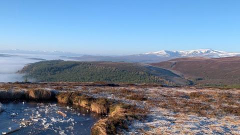 Snow topped mountains with an icy pond in the foreground and blue skies overhead