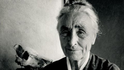 Black and white portrait of American artist Georgia O'Keeffe at her home in New Mexico, 1971. She has tied back hair and is looking past the person taking the photograph. 