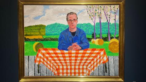 A vibrant painting showing a man in a blue jacket with brown swept back hair and round glasses who is sat at a table with an orange table cloth outside. 