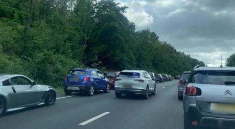 An unmarked police car with its blue lights on drives along the A38 in Devon to the scene of a crash. Both lanes of traffic have moved over to allow space for the vehicle to move through.