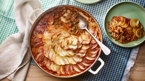 A large cast iron dish filled with veggie mince topped with sliced potatoes in a swirl pattern.