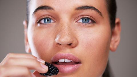 A close up of a young woman's face, she is holding a blackberry up to her lips.