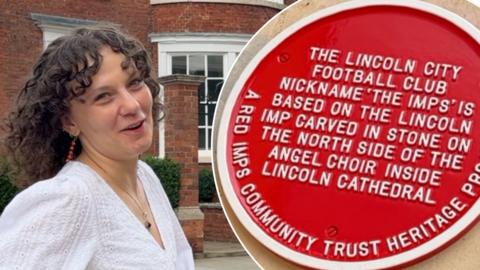 Young woman with short, brunette curly hair walks away from cam. Red plaque on Lincoln City can be seen.