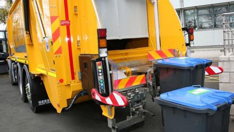A bin lorry is parked beside a building, ready for waste collection in an urban setting.