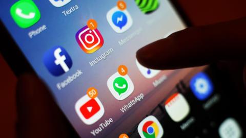 A smartphone screen with several brightly coloured icons, including green for Whats App and a green logo for the phone with a picture of a phone in white on it. There's a finger tapping the screen.