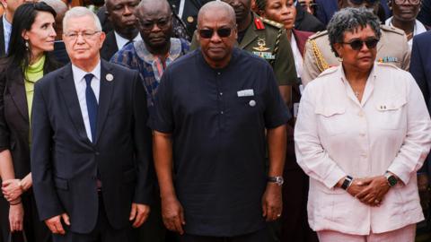 Ghana's President John Dramani Mahama, Barbados' Prime Minister Mia Amor Mottley and other dignitaries stand looking solemn.