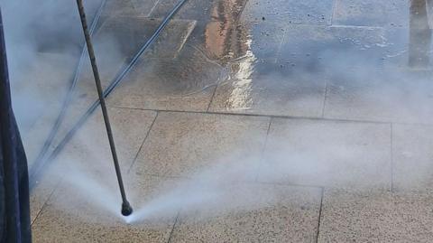 A thin water spray gun pointing down at a pavement cleaning it