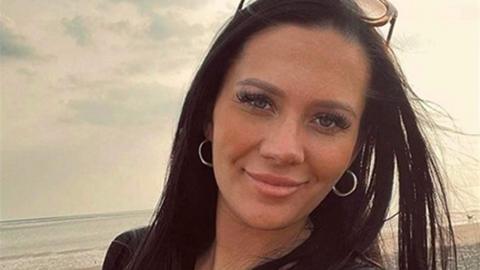 Kiena Dawes, with long black hair and silver hoop earrings, smiles as she is photographed on a beach.