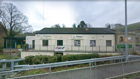 A white walled swimming pool building with signs for the swimming pool and fitness centre