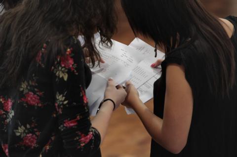 Two sixth form aged girls looking at pieces of paper with exam results on them. We cannot see their faces.