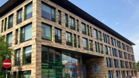 A large modern building of glass and brick in Wakefield city centre, with the names of towns in the district written on the windows. 