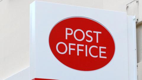 The Post Office logo, printed red and white on a sign outside.