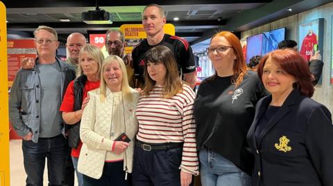 A group of four men and five women at the opening of the Candour and Communities exhibition. They looking at the camera.