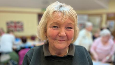 Shonette Mooney. A woman with short blonde hair. She is wearing a green polo top and green jumper. She is looking into the camera and is smiling.