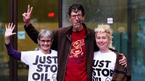 Mary Somerville, Stephen Simpson and Phillipa Green wearing Just Stop Oil T-shirts and waving outside court