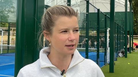 Former hockey Olympian Sophie Bray pictured at a padel court. Sophie has her hair tied back and is wearing a grey hoodie. 