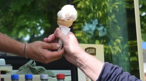 A person hands another person an ice cream from an ice cream van window