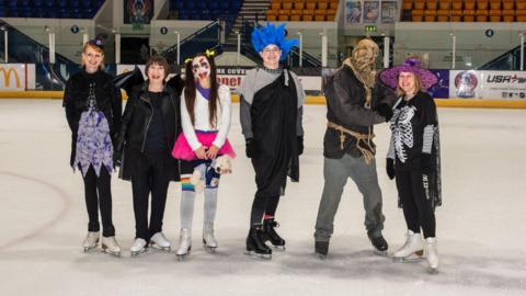 A group of people in halloween costumes posing on an ice rink
