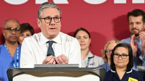 Starmer gestures while speaking with NHS staff in background