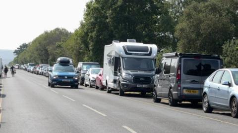 Cars and vans parked along one side of Ferry Road extending into the distance