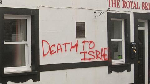 Red graffiti reading 'death to Israel' sprayed on a white pub building.