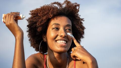 A young woman applies sunscreen to her face 