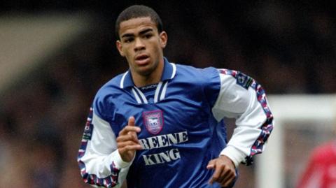 Kieron Dyer wearing an Ipswich Town football shirt while playing. It has the logo and the Greene King sponsor on the front of it.
