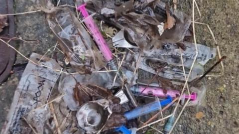 Discarded plastic syringes and needles on the ground.