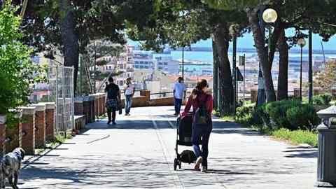 A woman pushes a pram as people walk along Viale Enrico Endrich in Cagliari, Sardinia, Italy