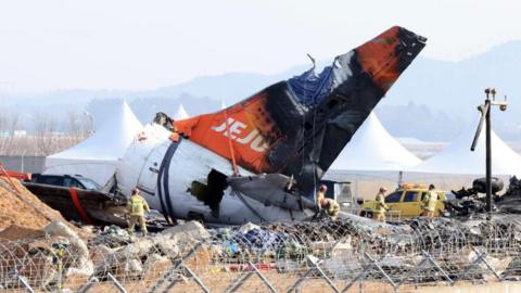 Firefighters remove tarpaulin sheets covering the debris of a Jeju Air passenger plane at Muan International Airport in Muan, southwestern South Korea, 13 January 2025, following its crash on 29 December 2024.