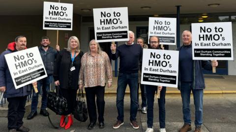 Eight members of East Durham Communities Standing Together group standing outside Durham County Hall and holding signs which read  No to HMO's in East Durham.