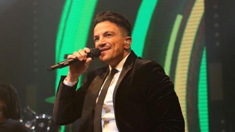 Peter Andre performing on stage in a black suite and tie. 