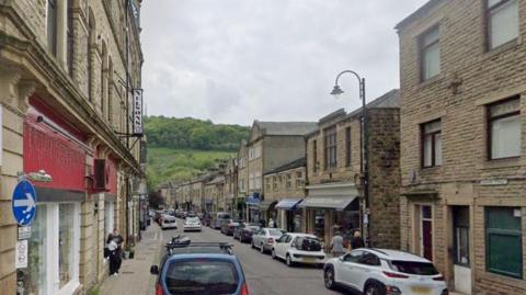 Crown Street in Hebden Bridge with shops and restaurants on either side and parked cars along the street