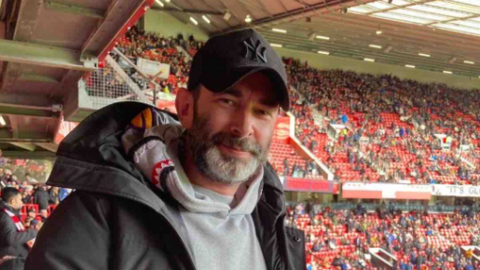 Mr Rimmer at football stadium - crowds in background wear red.