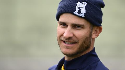 Sam Hain looks on wearing a blue hat with a Warwickshire cricket crest on the front