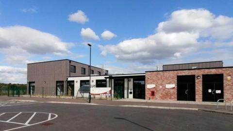 Brick and brown clad building with multiple single storey height doors and windows and double-storey building attached to its left