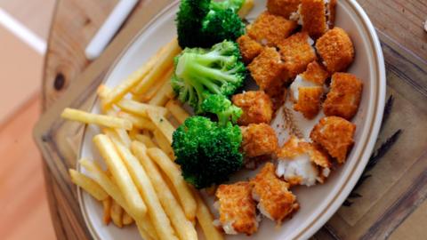 A plate of chips, chopped up fish fingers and broccoli.