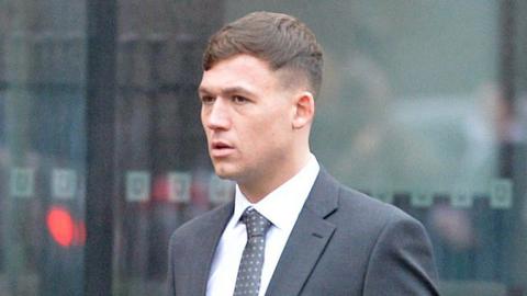 Joshua Findlay has short brown hair and wears a grey suit and tie with a white shirt