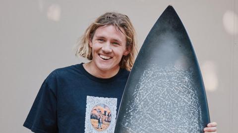 Kai McKenzie holds a surfboard