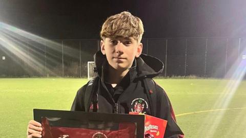 Ivan stood looking at the camera for a photo while holding a signed shirt.
