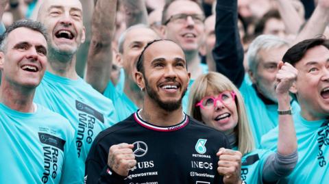 Lewis Hamilton dressed in a black Mercedes shirt alongside staff in turquoise shirts.