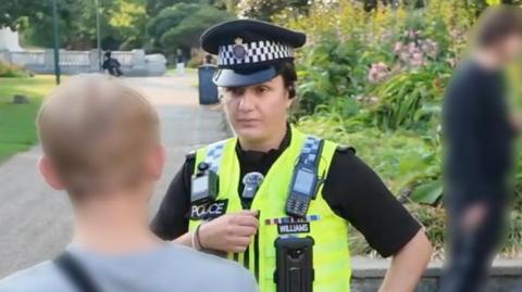 A woman and a police officer stood talking to a teenager in a park.